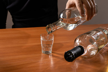 
A man pours vodka from a bottle into a glass. Alcoholism.