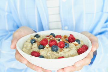 Faceless woman holds in hands breakfast, oatmeal porridge with berries and nuts