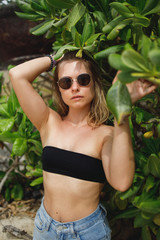 Blonde woman in black bathing suit and sunglasses on background of green tree