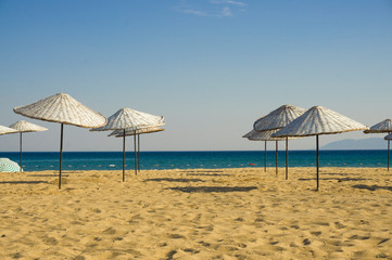 Empty beach and wicker umbrellas waiting for new summer season tourists. Beautiful summer holiday, vacation concept background. Inspirational landscape. Tourism and travel design. Hot summer is coming