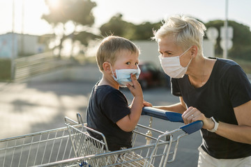 Mother joyfully playing with kid sitting in shopping cart. Both wearing protective face mask.