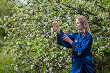 a girl practices Chinese gymnastics against of blooming Apple tree