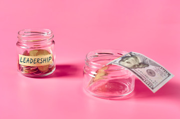 Glass jar with coins and inscription leadership lies on pink background
