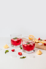 Refreshing strawberry smoothies, lemon slices and crushed ice on a gray background, vertical photo