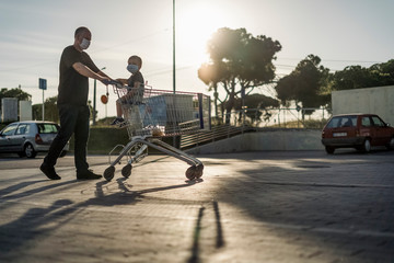 Obraz premium Father pushing shopping cart with his little son. Both wearing protective masks.