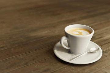coffee with milk on a plate accompanied by a metal spoon on a rustic table
