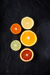 Sliced fresh ripe citruses. Lemon, lime, red orange and mandarin on a dark stone background. Top view with copy space