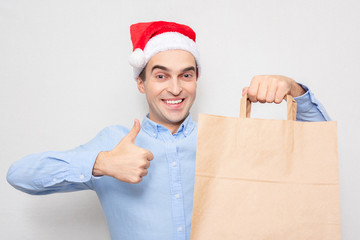 Concept of a new year. Man in Santa Claus hat with gift bag, man shows thumb up, portrait, white background, copy space