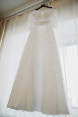 Wedding lace dress of the bride weighs on a wooden hanger. Cream cream dress. The morning of the bride. Visiting ceremony. Bride and groom. Wedding. Сocktail dress, evening dress.