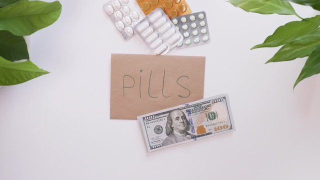 Top down view. Female hands count american money, dollars, and then put it on an envelope with the inscription, the word Pills. The girl is saving money for pills.