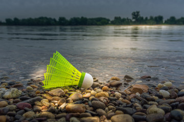 Fototapeta na wymiar Green plastic shuttlecock on a lake or river shore