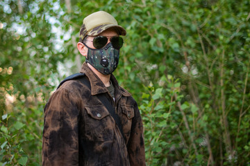 Obraz premium A man wearing respirator mask in sun glasses and a cap walking in the forest at COVID-19 period.