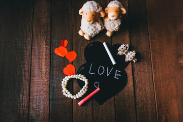 on a wooden background funny figures of sheep and black heart with the word love, valentines day