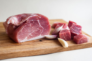 Fresh pork meat, pieces of different sizes on a wooden stand on a light background