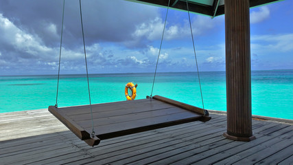 A delightful vacation in the middle of the ocean. A swing is suspended on a platform in the ocean. A place to relax in the shade and watch the colors of the aquamarine ocean and amazing cloudy scenery