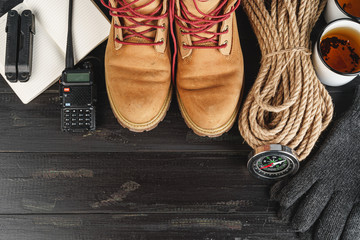 Hiking boots with equipment for hiking, cup of tea on wooden board