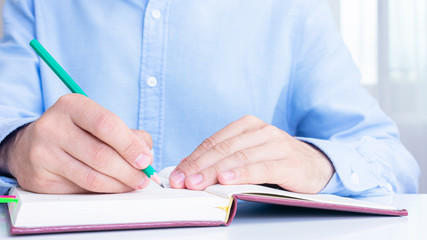 Man makes notes in a notebook, cropped image, close up