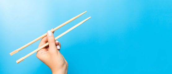Wooden chopsticks holded with female hands on blue background. Ready for eating concepts with empty space
