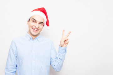 Guy in Santa Claus hat shows the gesture of peace, portrait, white background, copy space