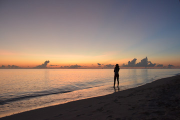 Girl in a hat walking on the beach at sunset.  Silhouette of a girl and the sea. Maldives.