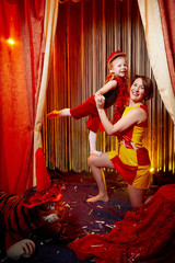 Family during a stylized theatrical circus photo shoot in a beautiful red location. Models mother and daughter posing as gymnasts on stage with curtain © keleny