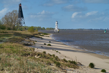 wooden black lighthouse on  in front of a white metal lighthouse far away at the beach of the...
