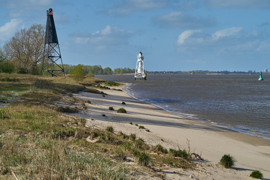 wooden black lighthouse on  in front of a white metal lighthouse far away at the beach of the island Elsflether Sand in the river Weser (Germany) on a sunny spring day