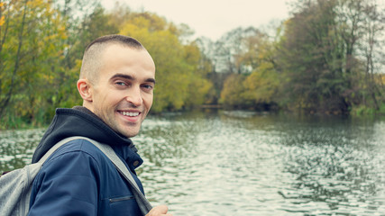 Fototapeta premium Attractive traveler man smiles and looking at camera, man in the background of a beautiful landscape, rear view, toned, 16:9