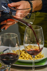Hand of a man holding a decanter and pouring red wine in a glass close up