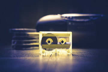 Transparent audio cassette tape lit by yellow and blue lamps. Retro tape recorder on the background. Retro audio. Hipster fashion concept