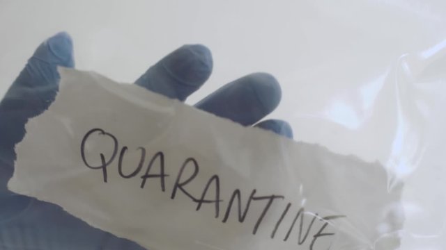 Hand with piece of paper with a word quarantine smacks against plastic isolation