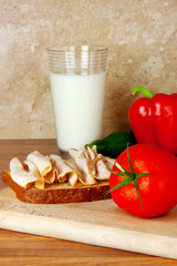 Tasty sandwich on a wholewheat bread with a glass of milk and vegetables on a background