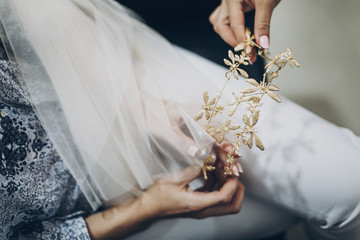 Stylish bride holding golden tiara with butterflies, morning preparations for wedding day. Bride in hair salon styling her hair with modern authentic wreath © sonyachny