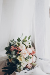 Modern wedding bouquet. Stylish wedding bouquet of pink roses and green eucalyptus on white soft tulle close up. Wedding arrangements and floristics