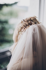 Stylish bride with golden tiara with butterflies and veil, morning preparations for wedding day. Back view. Bride in hair salon styling her hair with modern authentic wreath