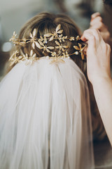 Hair stylish putting on stylish bride golden tiara with butterflies, morning preparations for wedding day. Bride in hair salon styling her hair with modern authentic wreath and veil