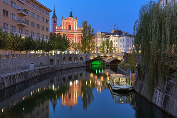 Fototapeta na wymiar Ljubljana, Slovenia. Evening view on Franciscan Church of the Annunciation and Triple Bridge across the Ljubljanica River. Latin motto on the facade of the church reads: Hail, full of grace!