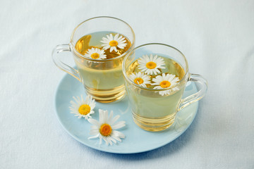 Herbal tea with fresh chamomile flowers in glass teacup on blue plate, seasonal colds flu alternative treatment, antidepressant and a remedy stomach cramps