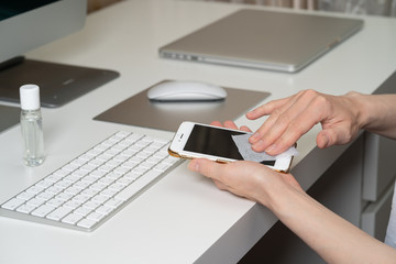 Close up of woman's hands in gloves wiping smartphone screen with disinfectant cloth