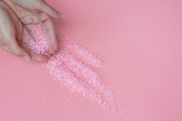 Himalayan salt on a pink background spills from the hands of a woman. Pink bath salt