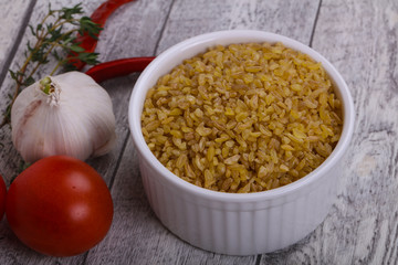 Raw bulgur in the bowl with tomatoes and garlic