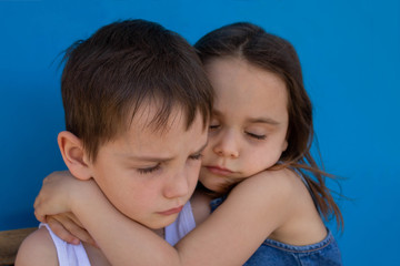 Little upset brother and sister. Isolated on a blue background. The concept of family love.