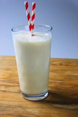 Tall glass with milkshake and two paper stripey straw on a rustic, wooden background 