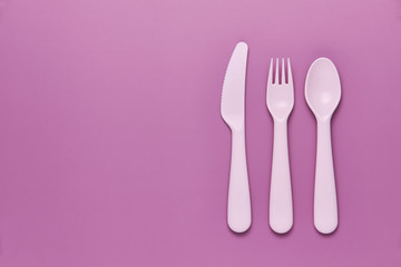 Plastic purple cutlery set with purple background. Top view