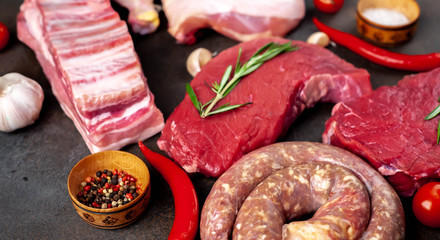 Various types of grill and barbecue. Raw beef steaks, sausages, pork ribs, chicken legs with spices on a stone background