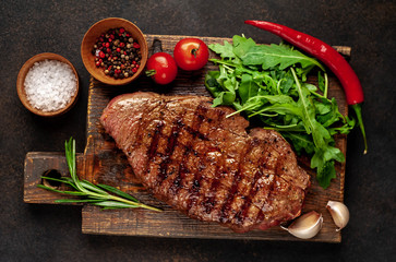 grilled beef steak with spices and herbs on a cutting board on a stone background