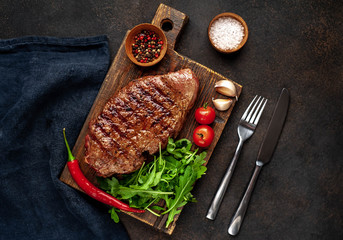 grilled beef steak with spices and herbs on a cutting board on a stone background