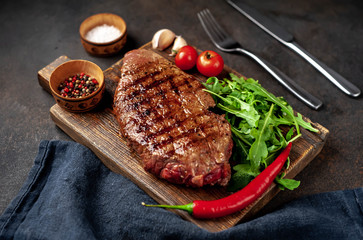 grilled beef steak with spices and herbs on a cutting board on a stone background