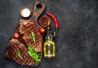 Two grilled beef steaks with spices and herbs on a cutting board on a stone background with copy space for your text