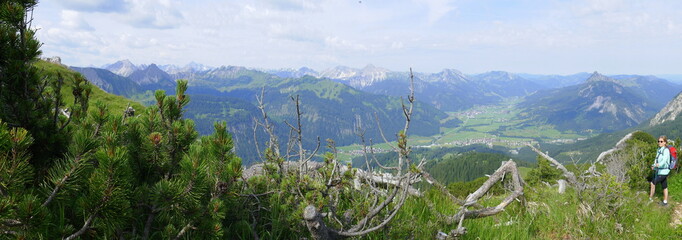 Panoramabild über das Tannheimer Tal und die Bergkette mit einer Wanderin am rechten Bildrand